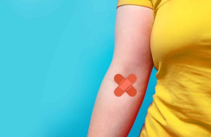 Blood donation. Blood donor woman in yellow T-shirt with patch bandage after giving blood on a blue background. World blood donor day and save life concept.