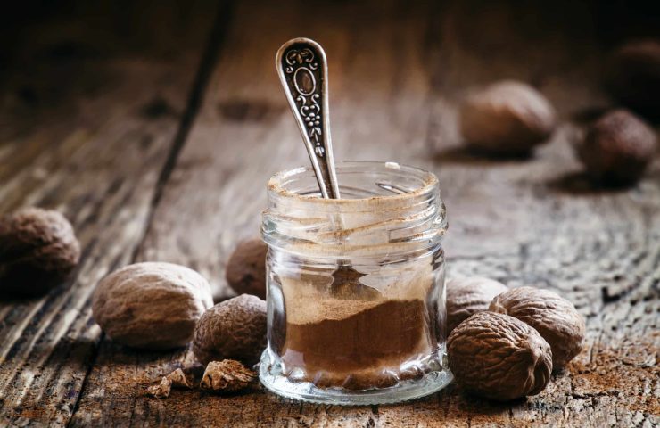 Ground nutmeg in a jar and whole nuts on an old wooden backgroun