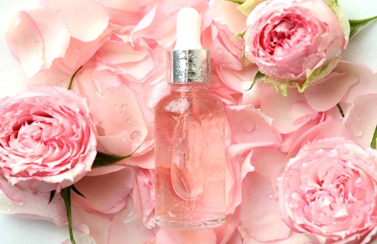 Bottle with rose essential oil on rose petals background