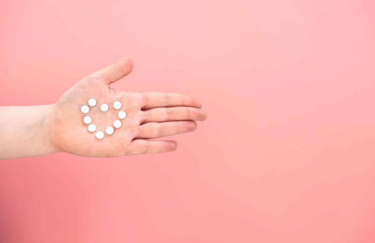 Pills in the shape of a heart on a female palm, pink background.