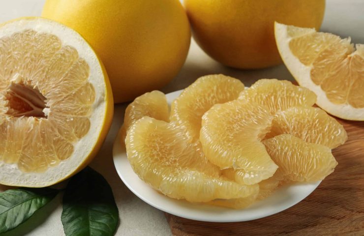 Ripe pomelo and plate with pomelo slices on white textured backg