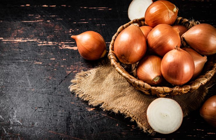 Whole onions in a basket with halves of onions on the table.